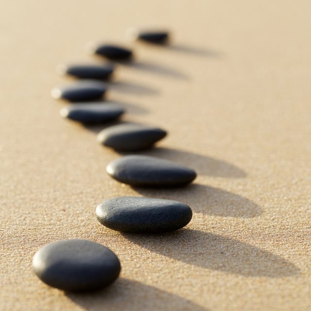 set of hot stone on white sand calm beach in backbone shape. selective focus, spa concept